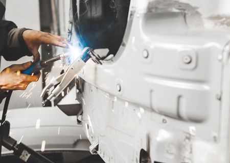 A man is welding a white car in a garage.