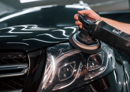 A person is polishing the headlights of a black car.