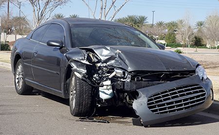 Damaged grey coupe car after a collision; front end crumpled, on a road.