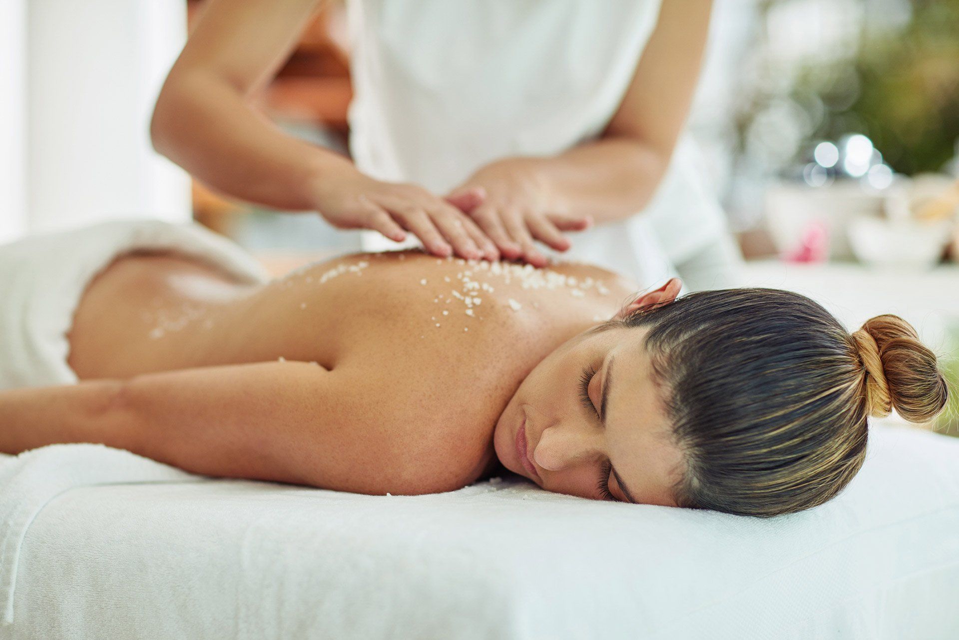 A person receives a spa back treatment with exfoliating scrub, lying on a massage table.