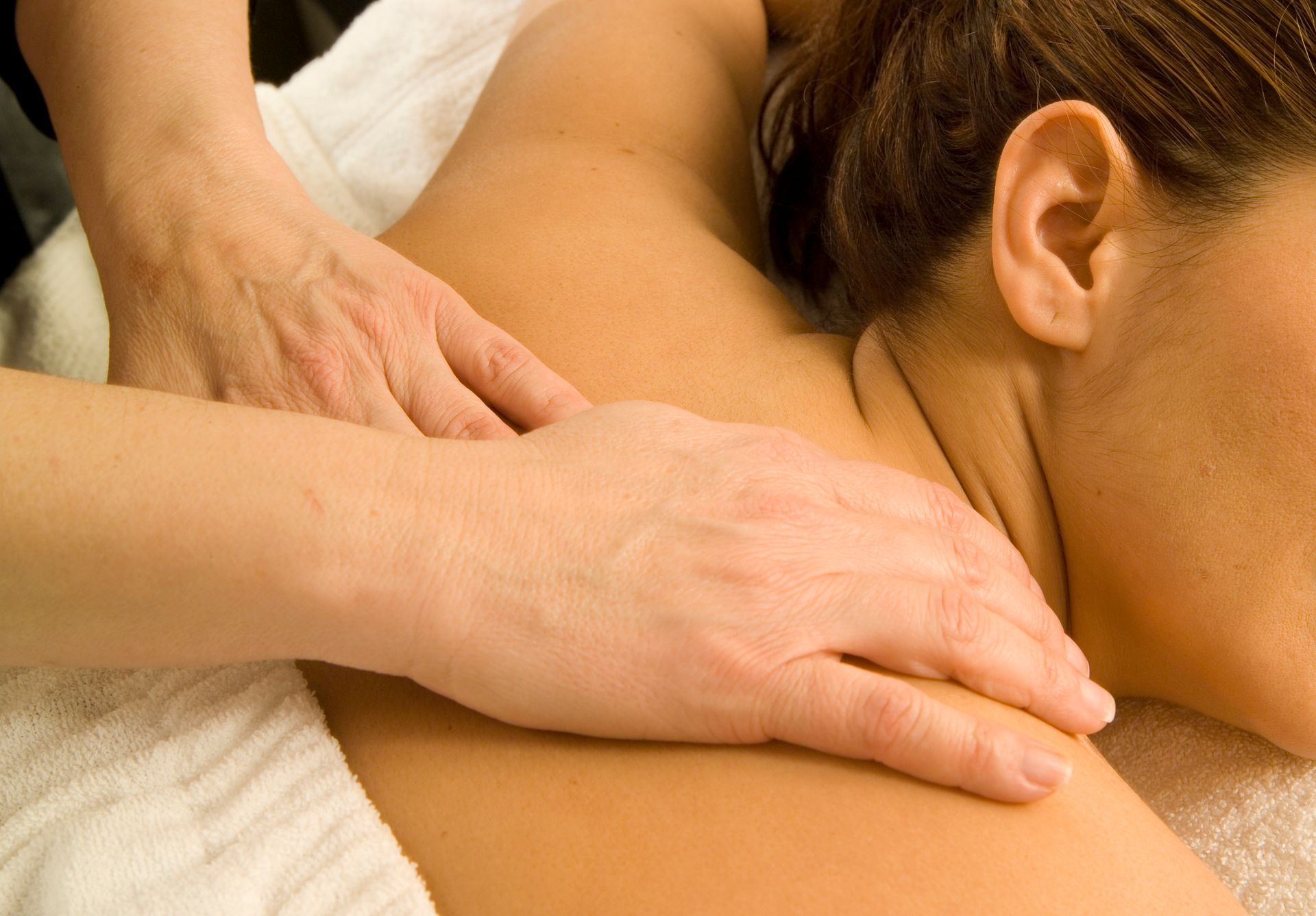 A close-up view of hands performing a massage on the shoulder and upper back area of a person lying on a white towel.