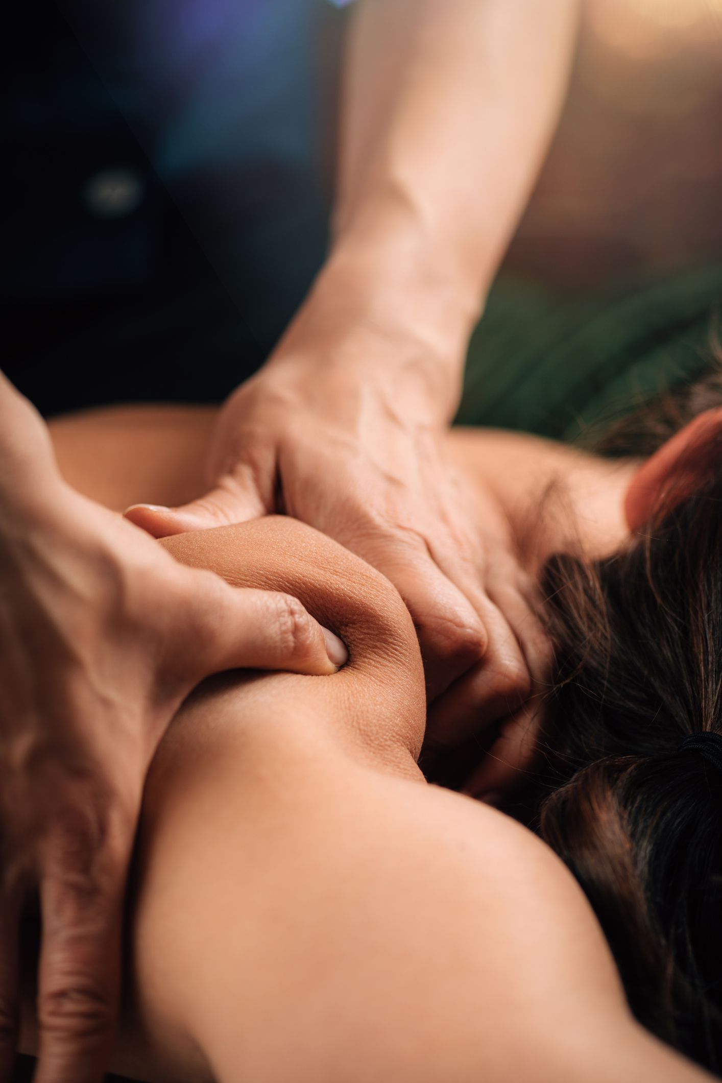 A close-up view of hands performing a deep tissue massage on a person's shoulder and upper back.