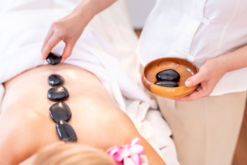 A therapist places smooth, dark heated stones along a client’s back during a professional spa treatment.