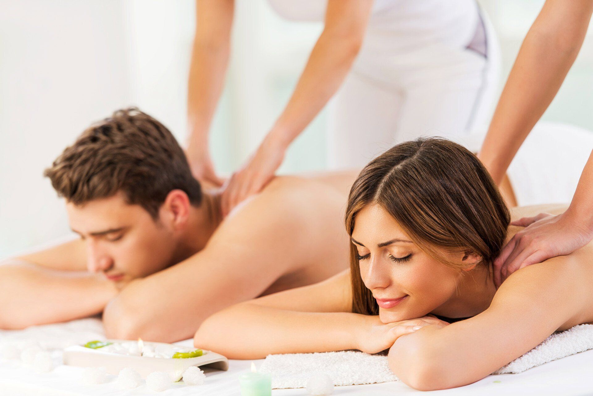 A couple relaxing on massage tables while receiving shoulder massages in a spa setting.