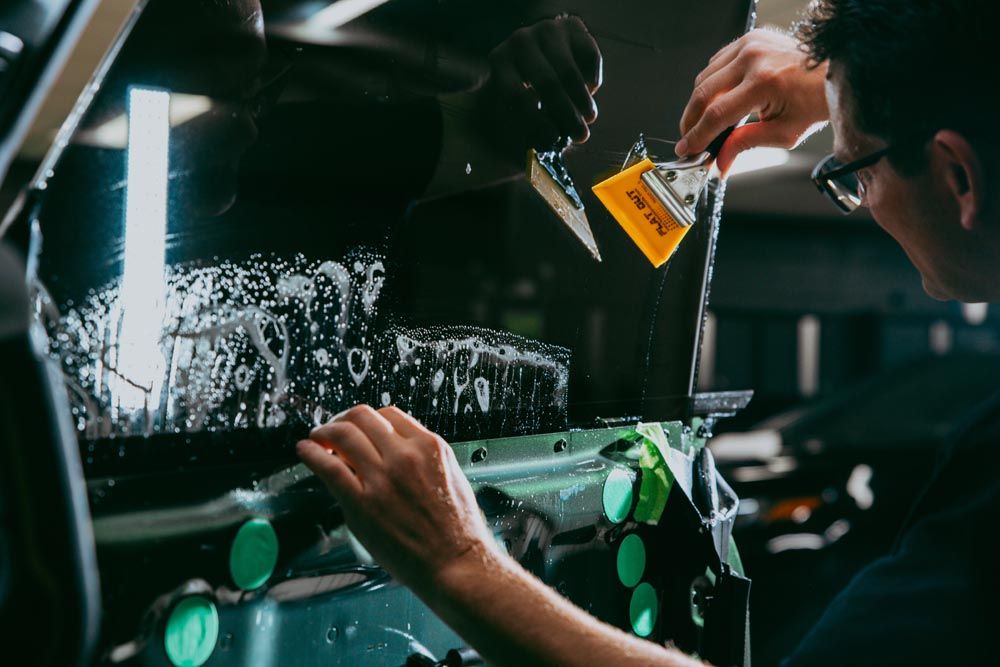 A man is applying tinted glass to a car window.