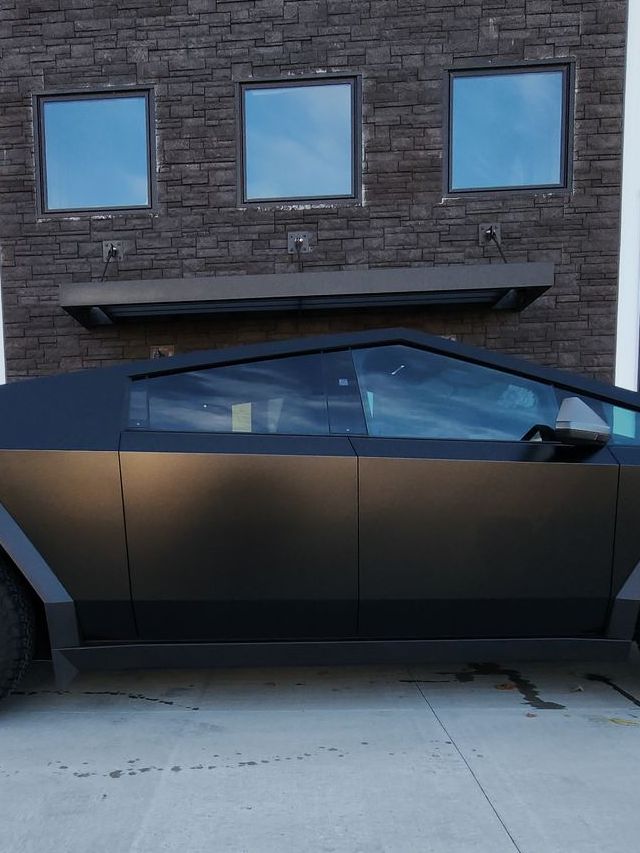 A person wearing black gloves is polishing a black car