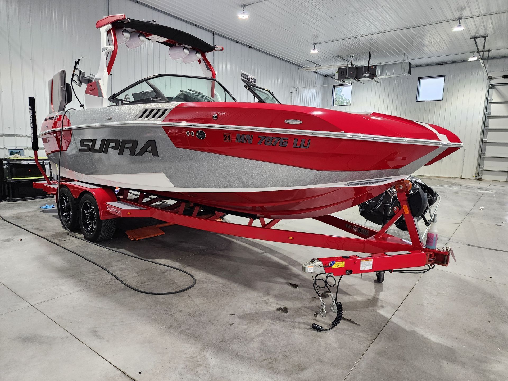 A red boat is parked in a garage on a trailer.