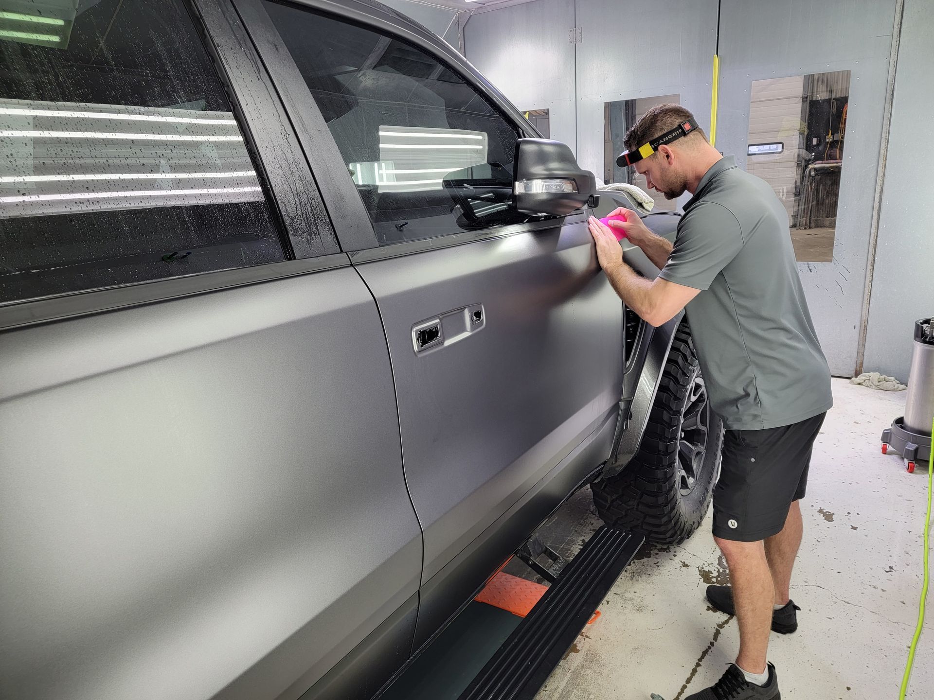 A man is wrapping a black truck in a garage.