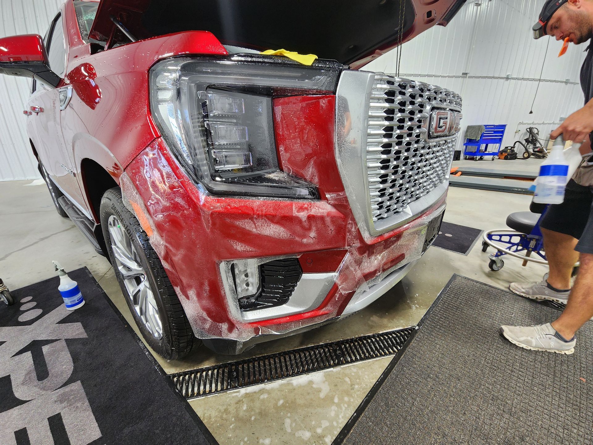 A man is covering the front of a red gmc truck with plastic wrap.