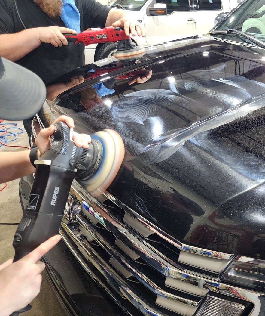 A man is polishing the hood of a black car