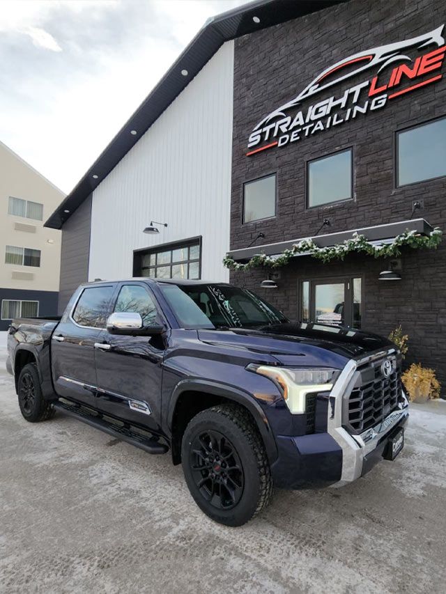 A blue truck is parked in front of a building that says straight line detailing.