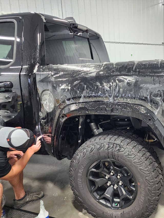 A person wearing black gloves is polishing a black car