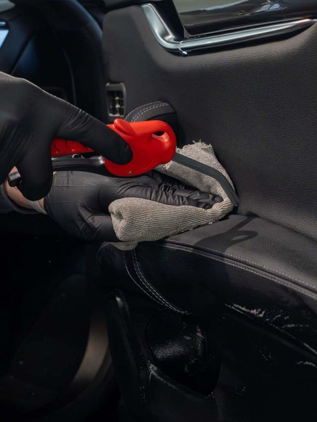 A person wearing black gloves is polishing a black car