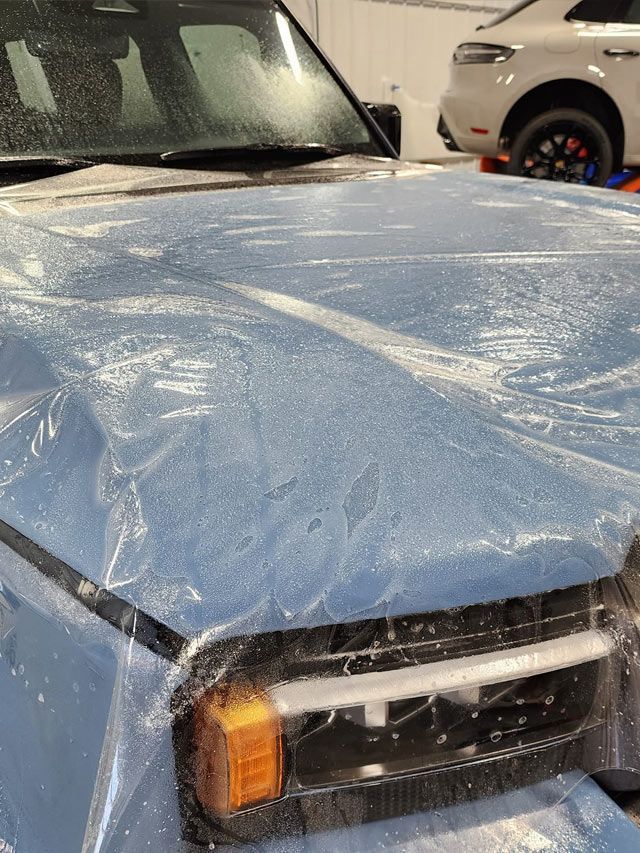 A car is covered in plastic wrap in a garage.