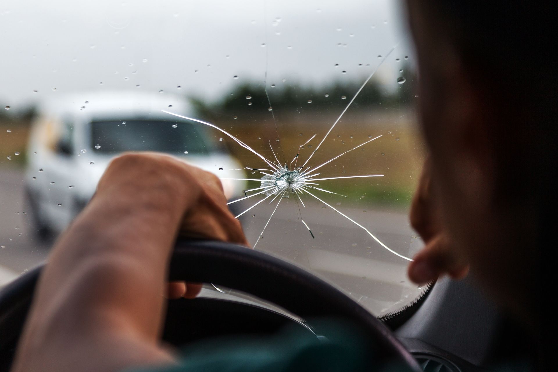 A man is driving a car with a broken windshield.