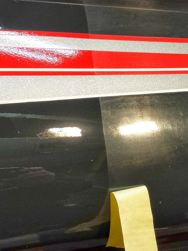A person wearing black gloves is polishing a black car