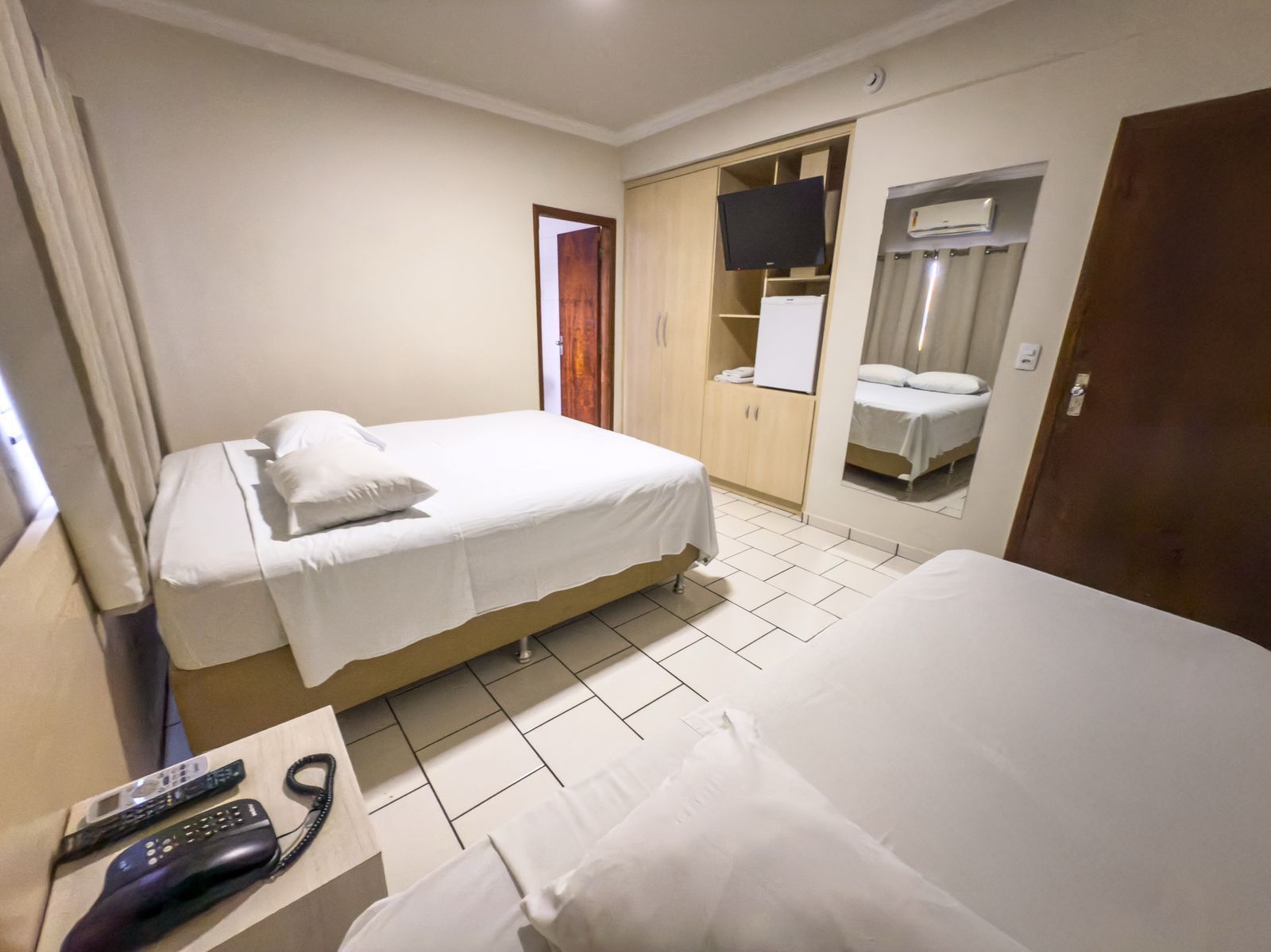 Um quarto de hotel com duas camas, uma televisão e um espelho.