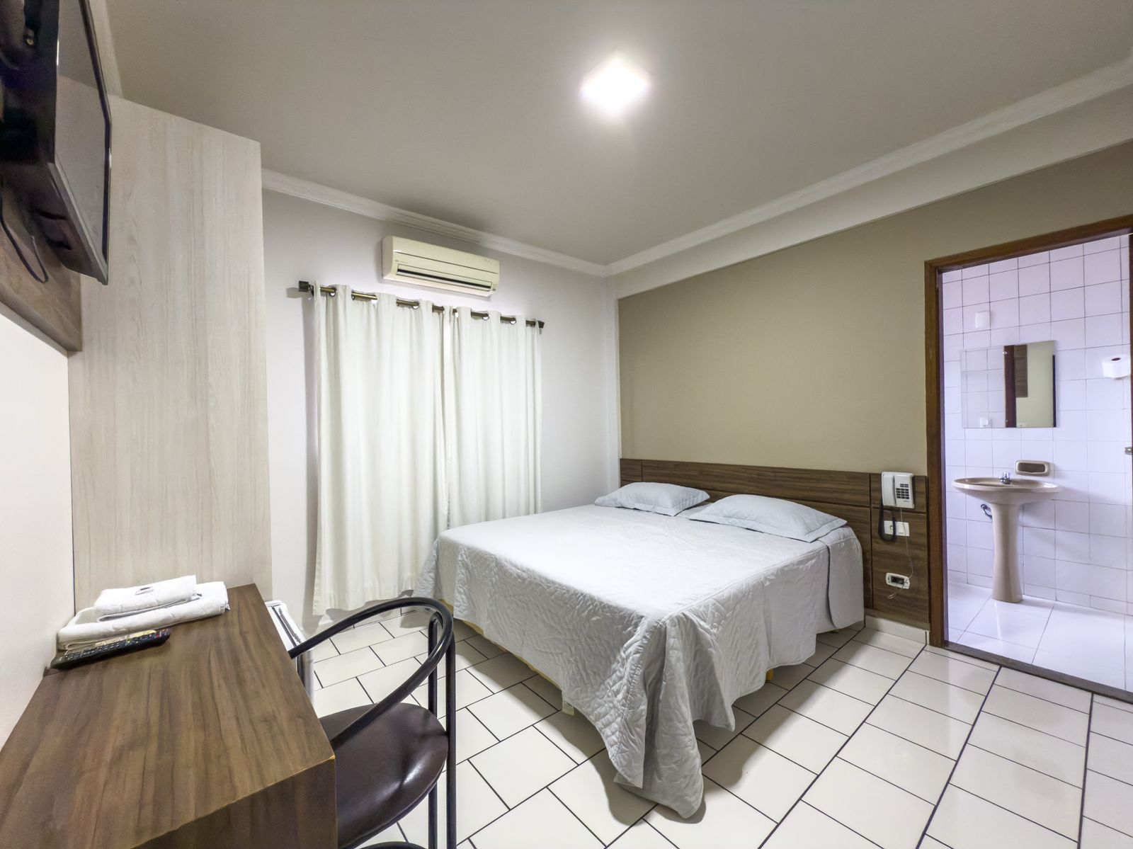 Um quarto de hotel com uma cama, escrivaninha, cadeira e televisão.