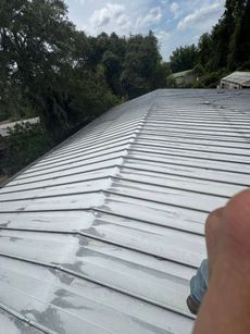 Metal roof on a house, with ridgeline running left to right, partially coated in a gray material.