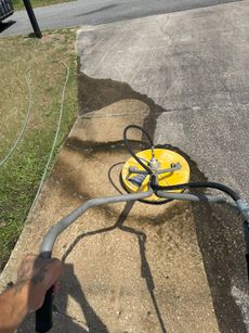 A person pressure washing a concrete surface using a yellow surface cleaner outdoors.