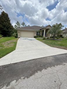 Beige house with concrete driveway under a cloudy sky.