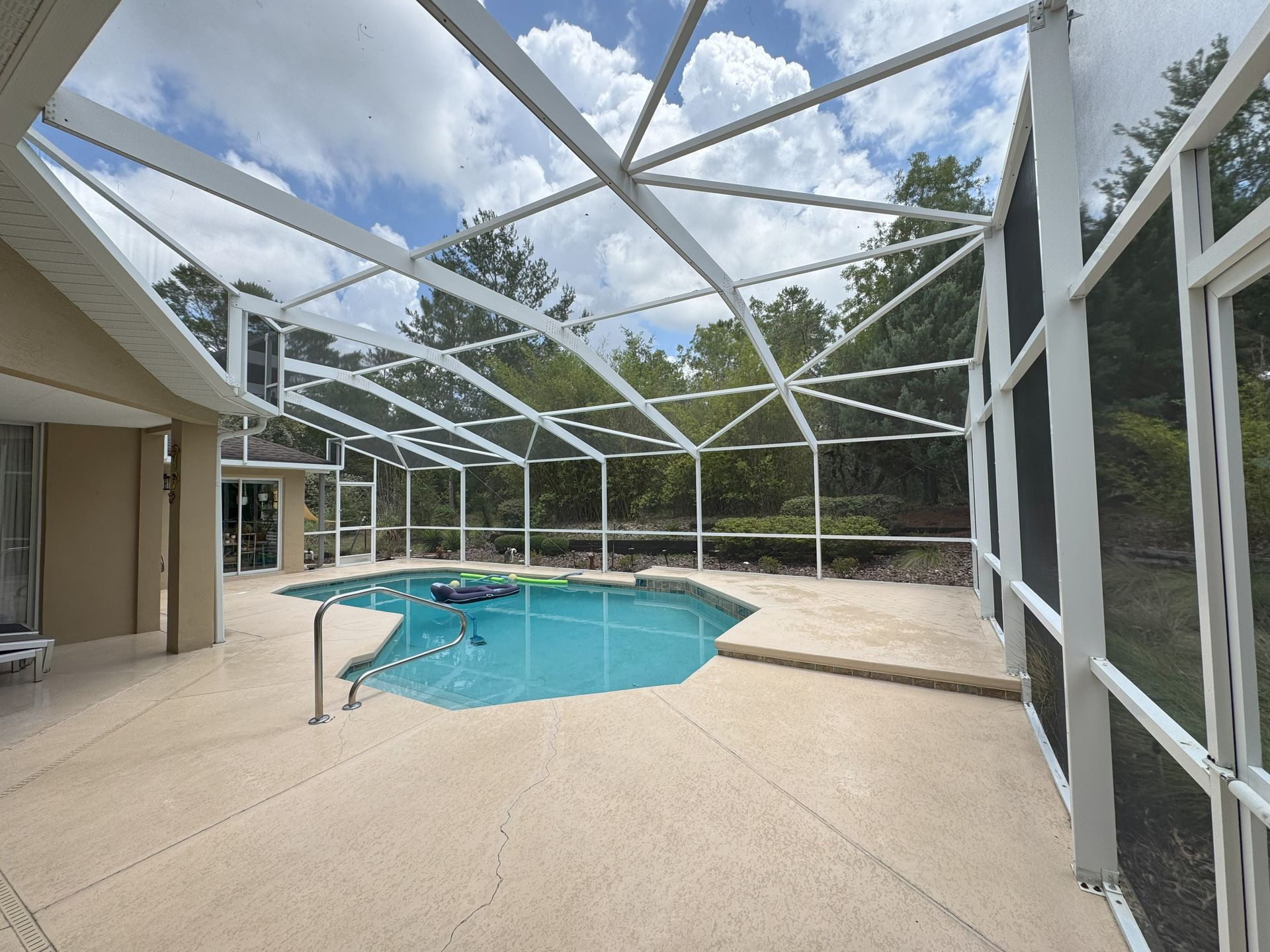 Pool enclosed by white screened structure; blue water; beige patio; trees visible in background.