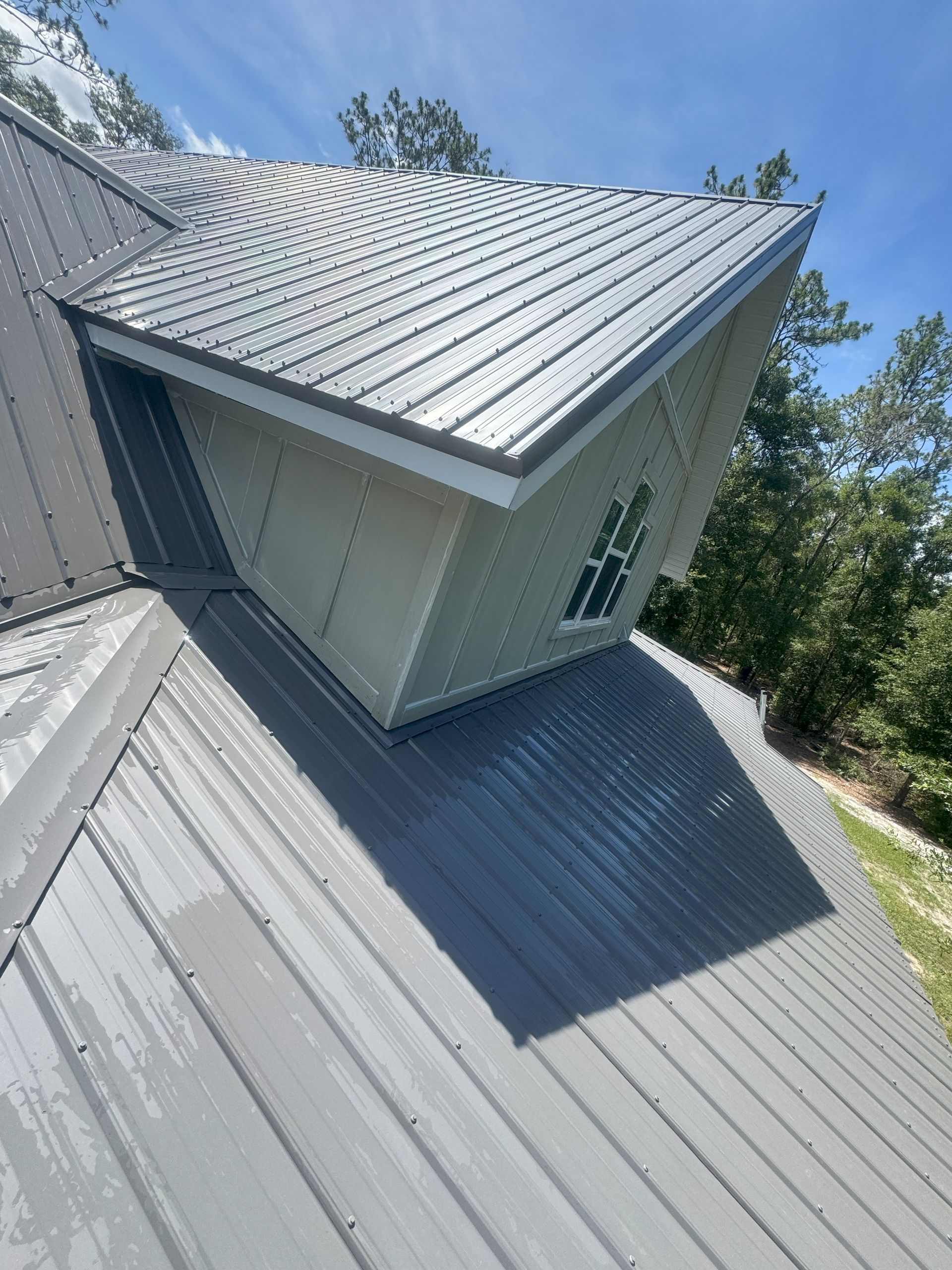 Gray metal roof with a dormer and a window against a blue sky.