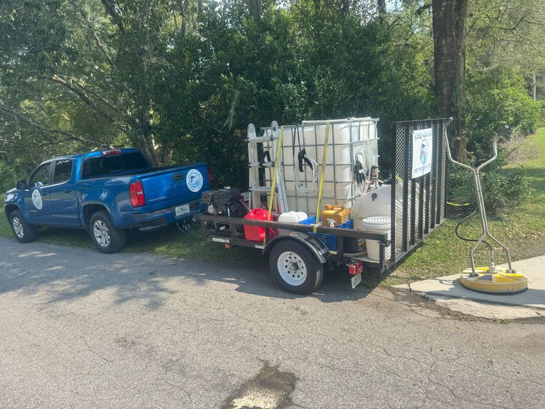 Blue truck towing a trailer with pressure washing equipment parked on a paved surface.