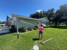 Woman power washing a house exterior on a sunny day with an American flag in the yard.