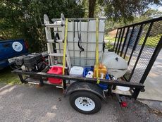 A trailer with a pressure washing setup including a water tank, ladder, and various containers.