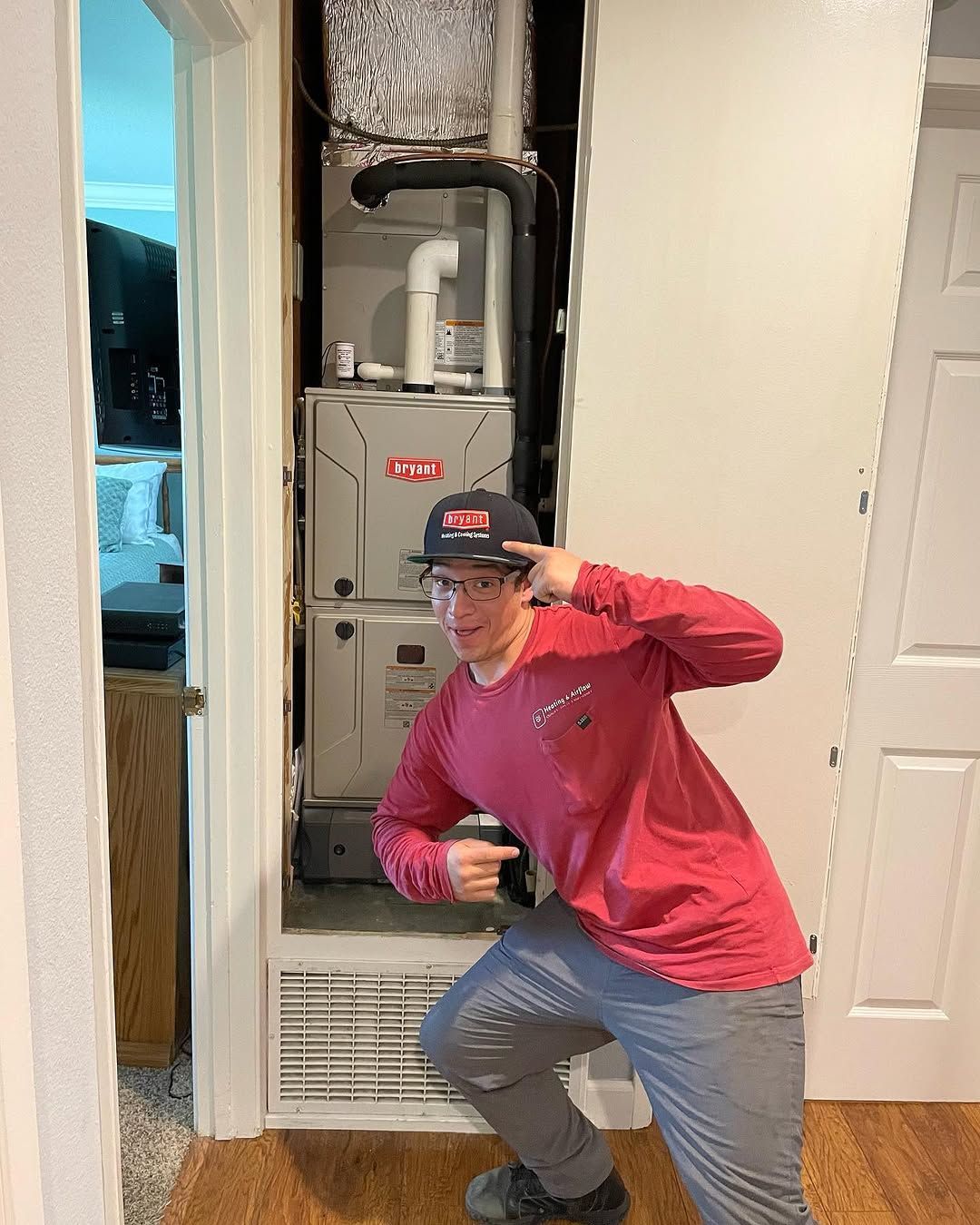 A man is kneeling in front of a furnace in a closet.