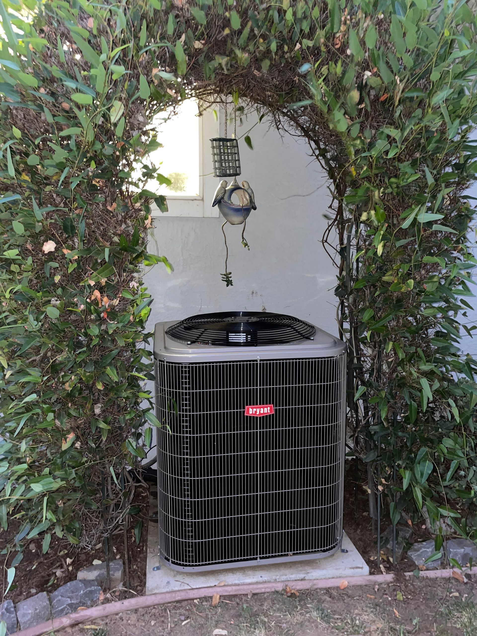 A black air conditioner is sitting in the middle of a bush.