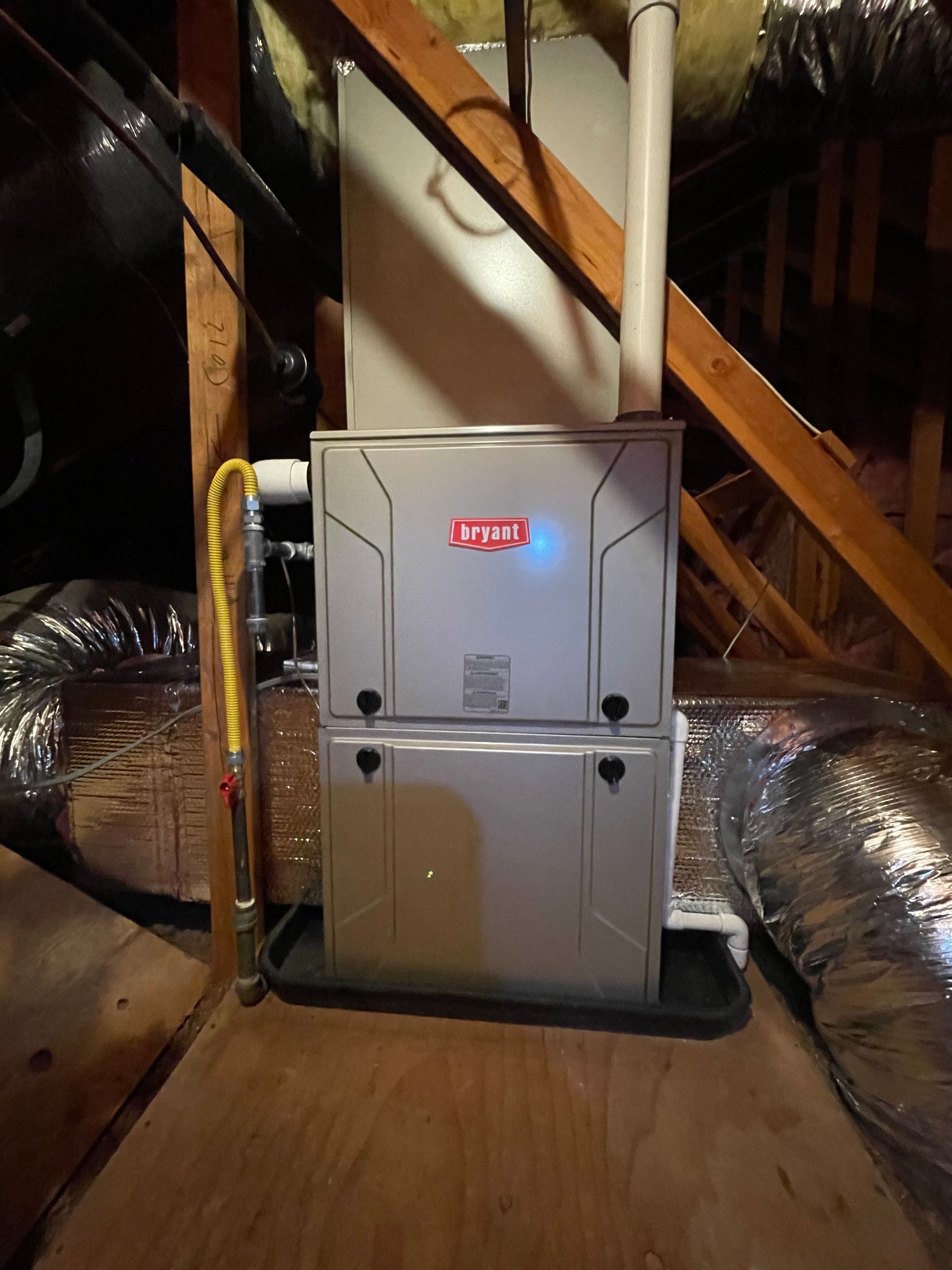 A furnace is sitting in the attic next to a staircase.