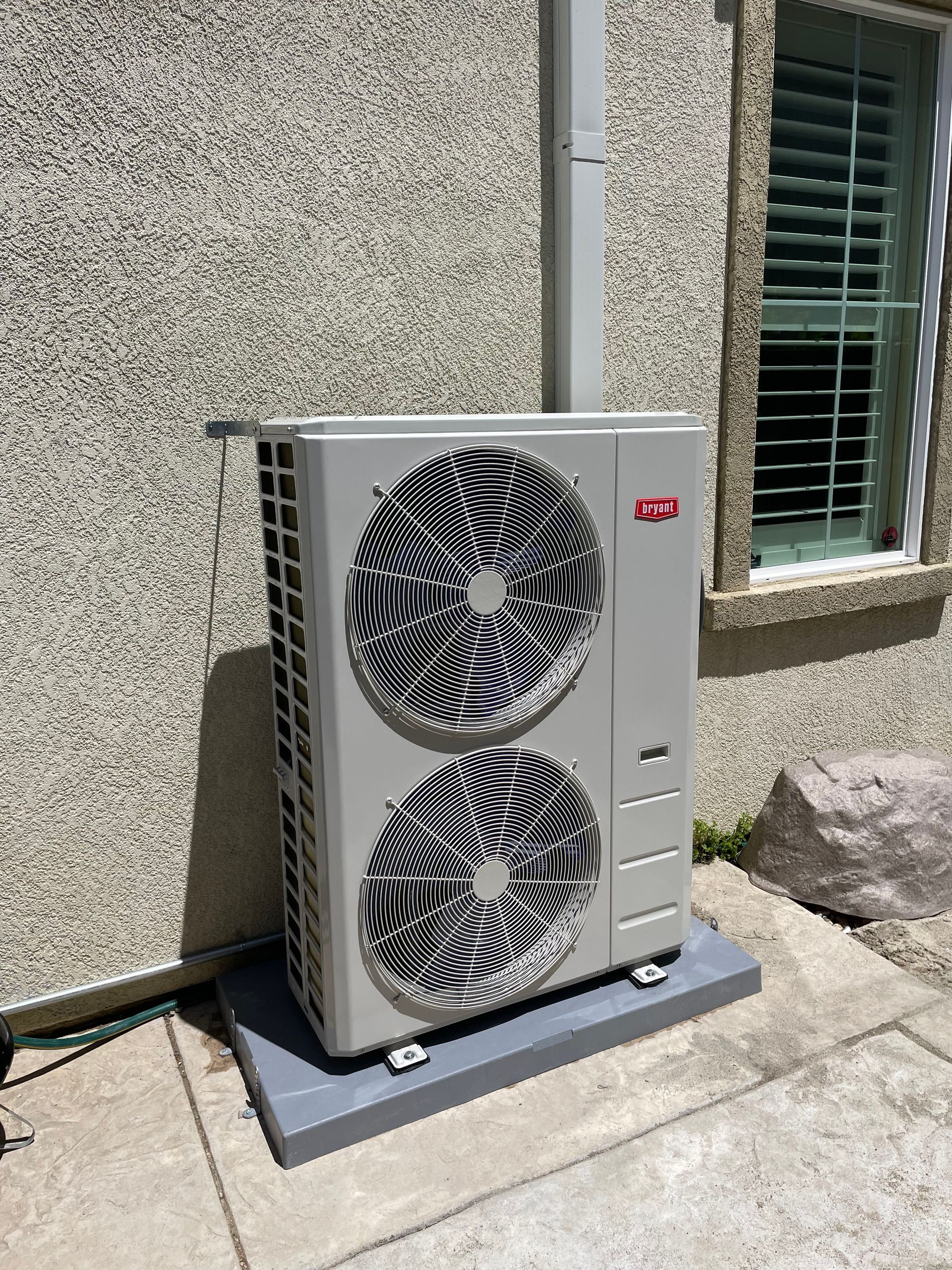 A large air conditioner is sitting outside of a building next to a window.