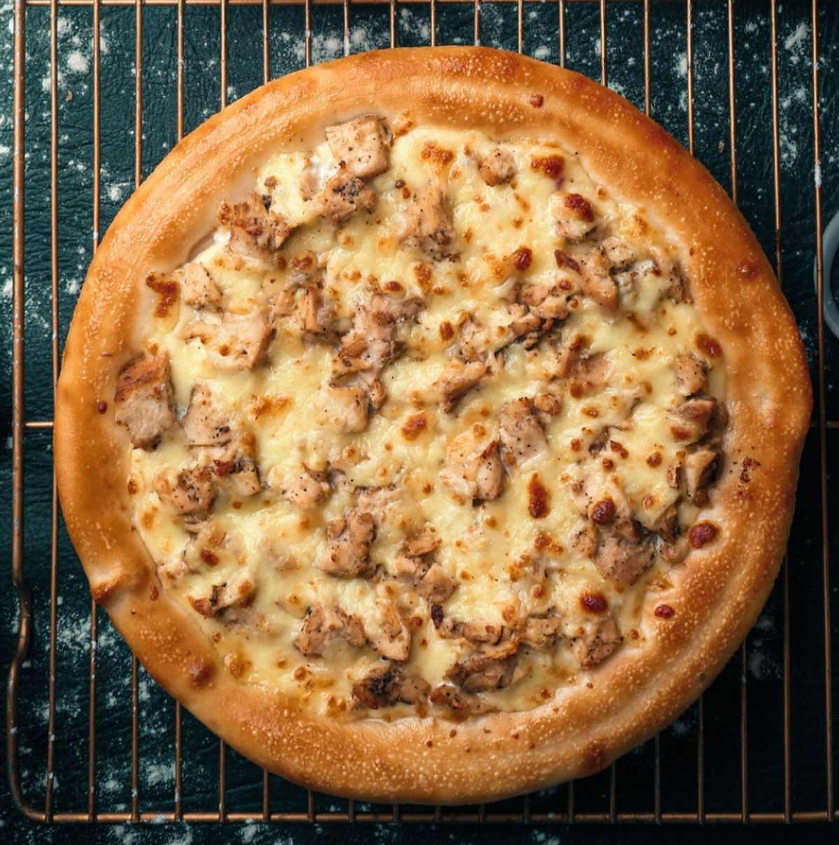 A pizza with chicken and cheese is sitting on a cooling rack.