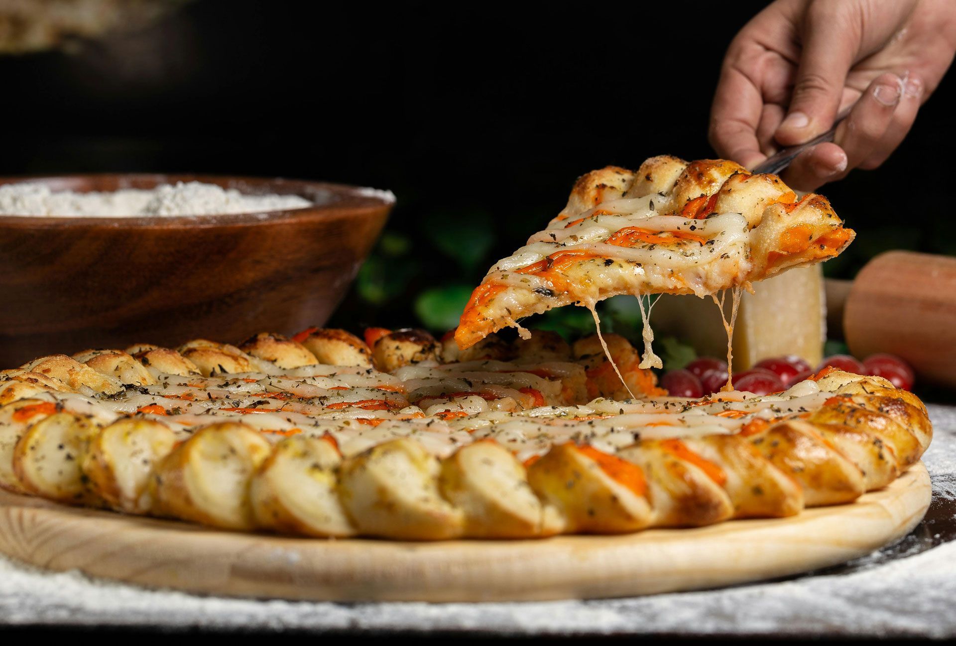 A person is taking a slice of pizza from a pizza on a wooden cutting board.