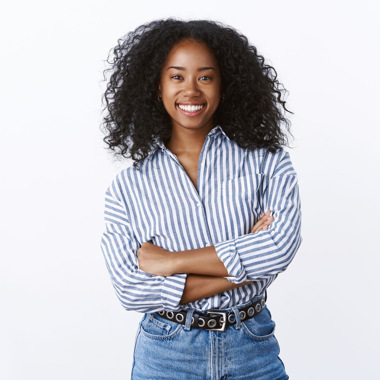 A woman wearing a striped shirt and jeans is smiling with her arms crossed