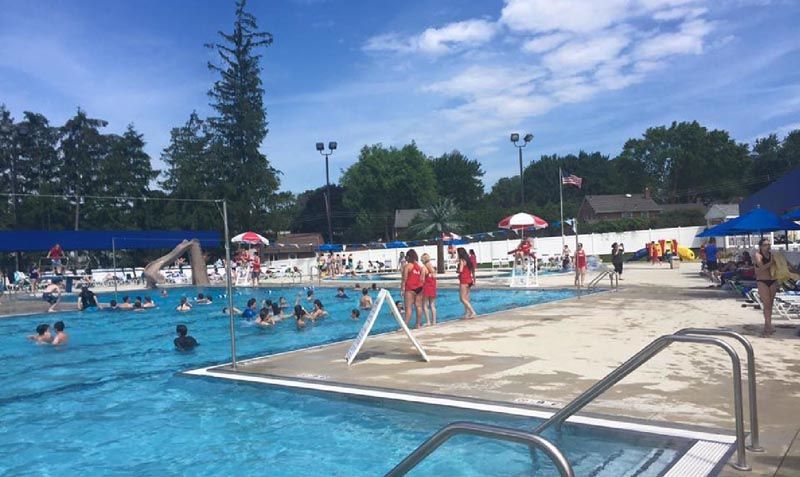 A crowded outdoor pool on a sunny day. People swim and stand around.
