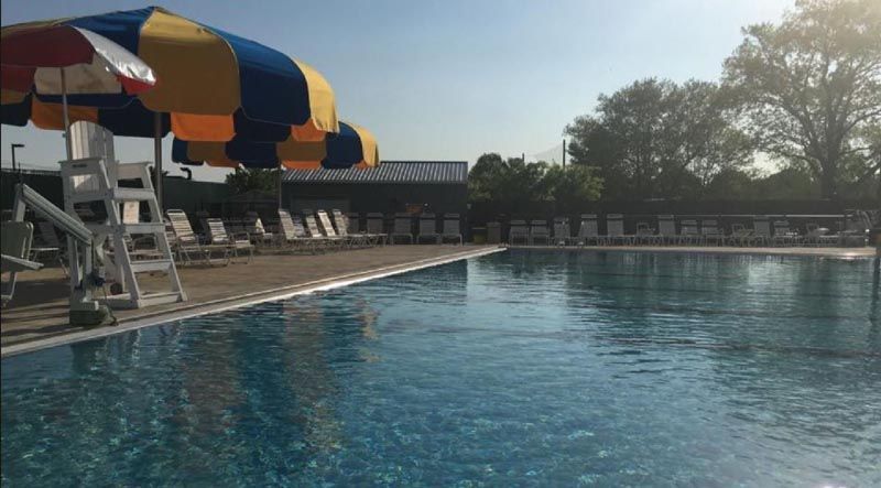 Poolside scene with a colorful umbrella, lifeguard stand, lounge chairs, and clear blue water.