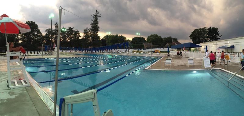 An outdoor swimming pool with lanes and a lifeguard stand under a cloudy sky.