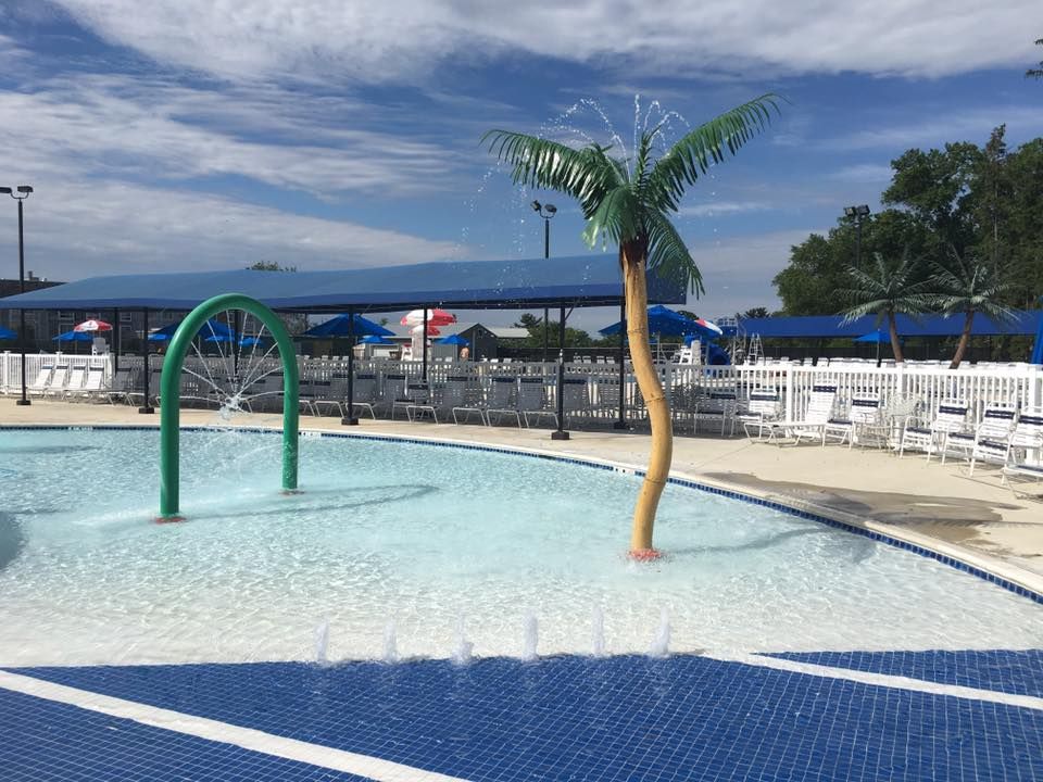 Pool with water features, palm tree, seating, and blue accents against a cloudy sky.