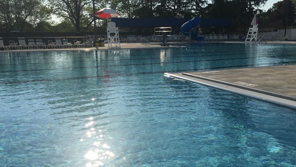 Pool with lifeguards, umbrella, and water slide on a sunny day.