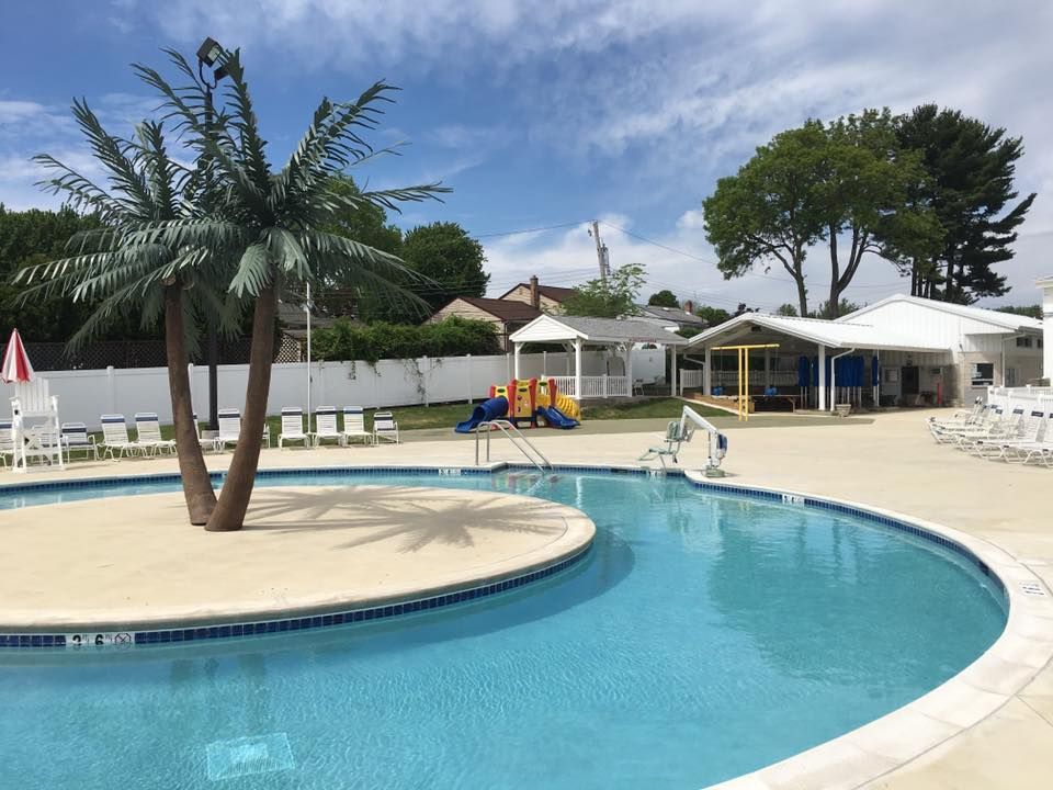 Pool with palm tree island, playground, and covered structures on a sunny day.