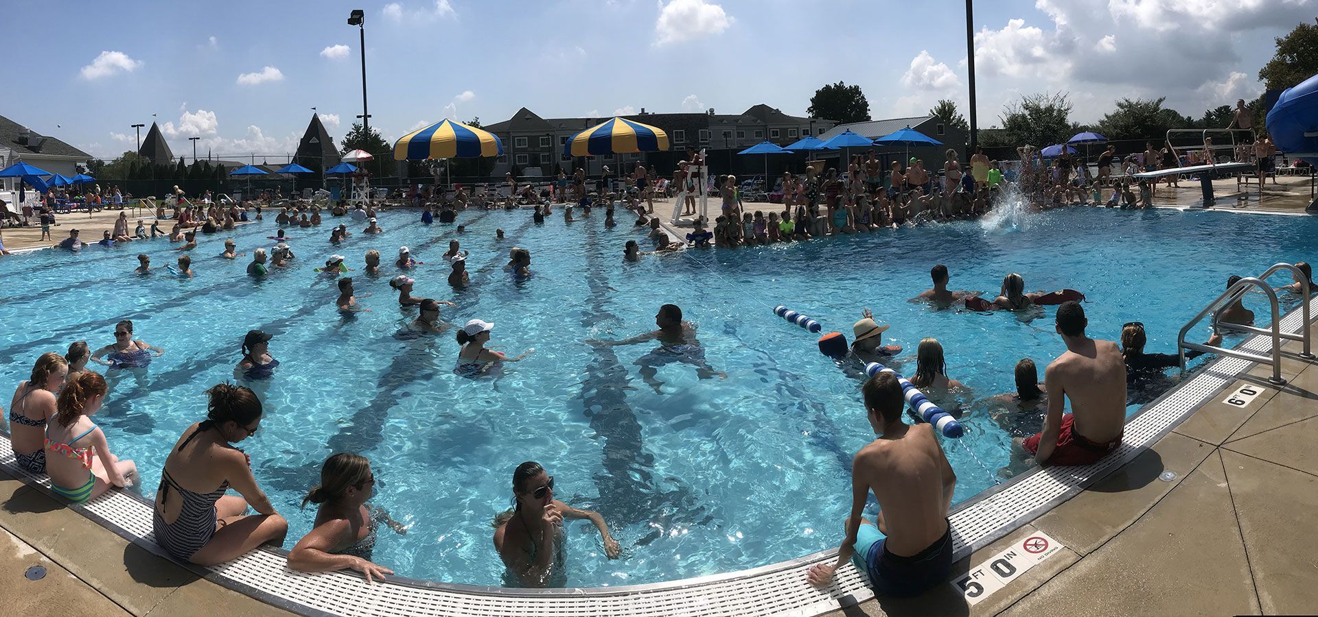 People swimming in a crowded outdoor pool on a sunny day.