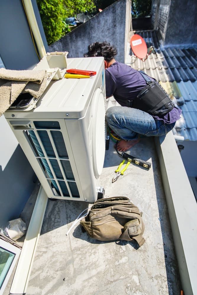 A Technician Crouched on a Rooftop Installs an Air Conditioning Unit