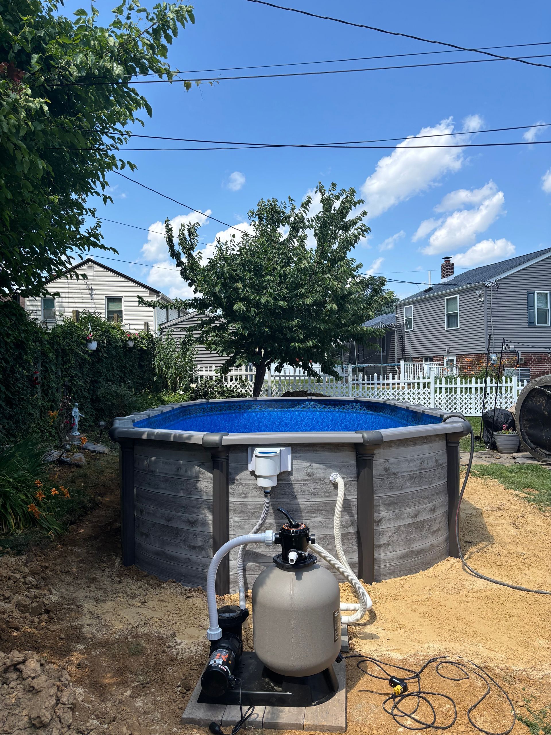A large swimming pool is sitting in a backyard next to a tree.