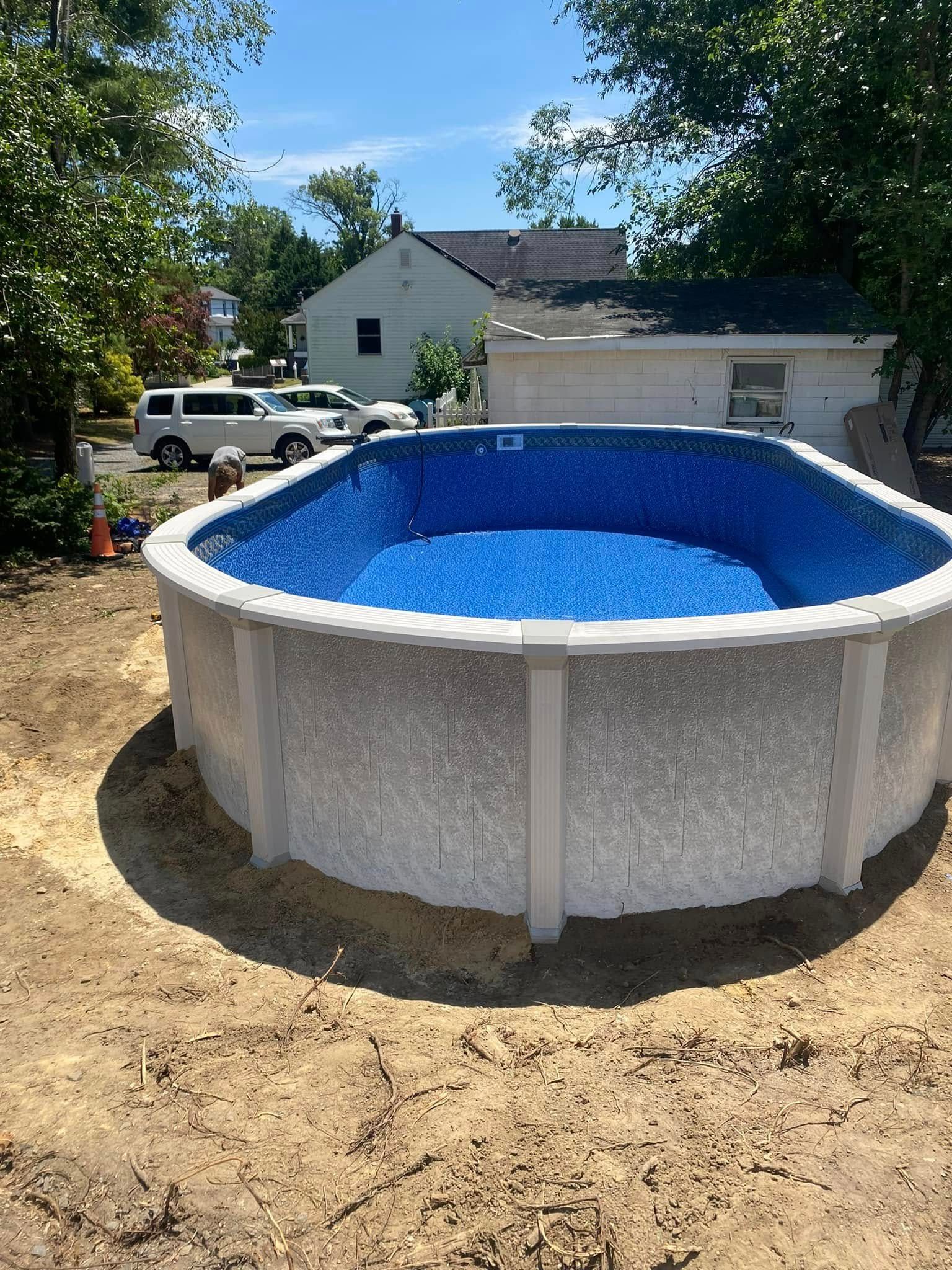 A large swimming pool is sitting in the middle of a dirt field in front of a house.