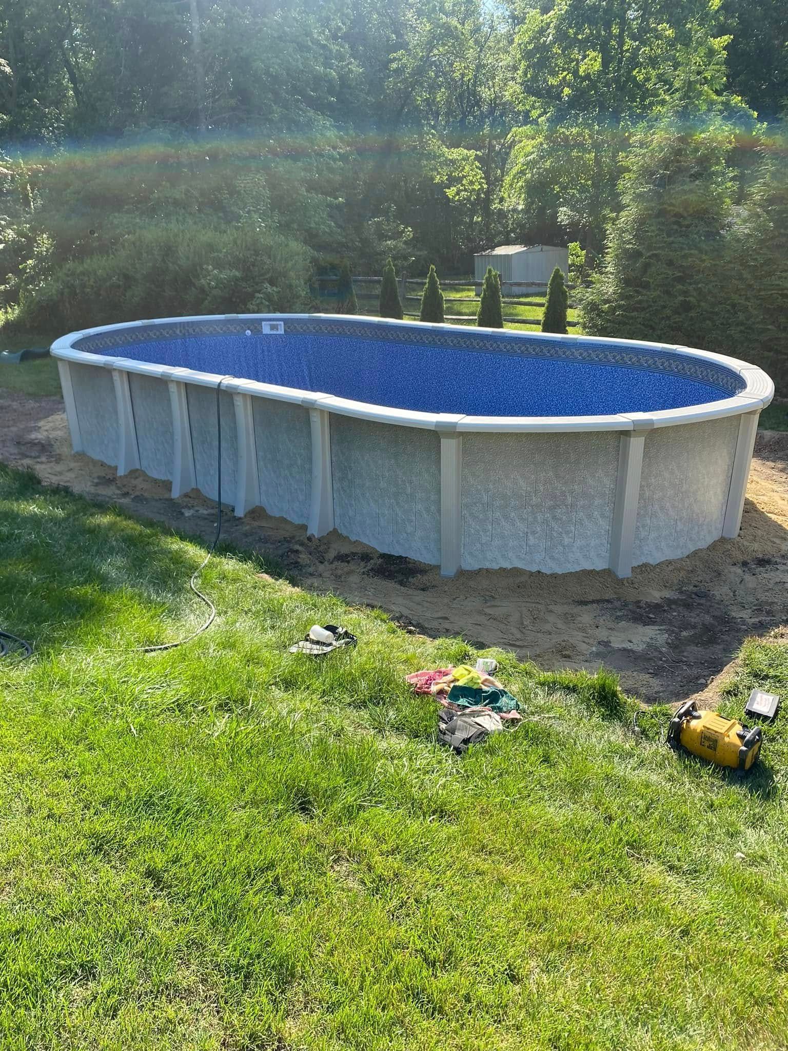 An oval swimming pool is sitting on top of a lush green lawn.