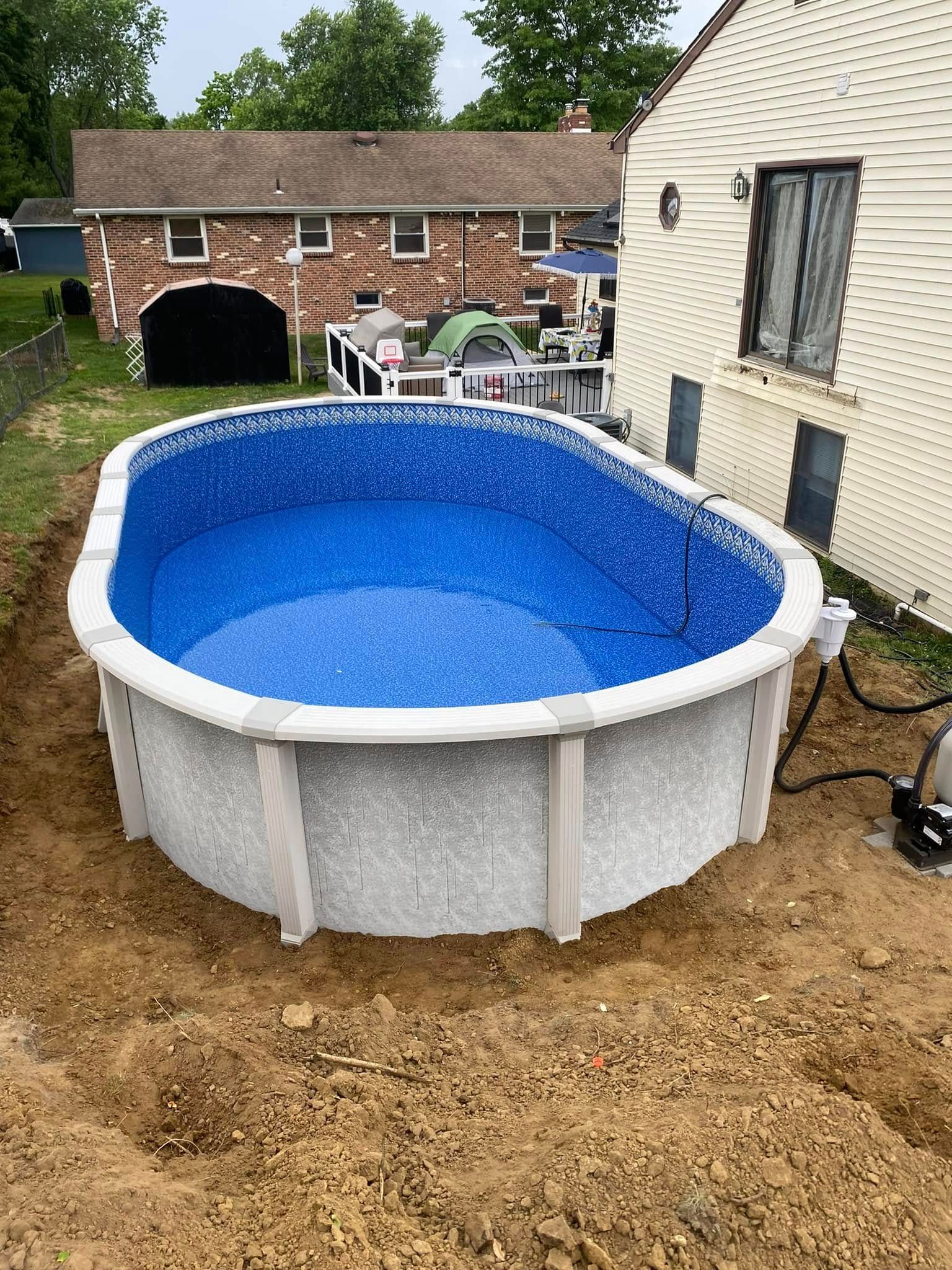 An oval swimming pool is sitting in the dirt in front of a house.
