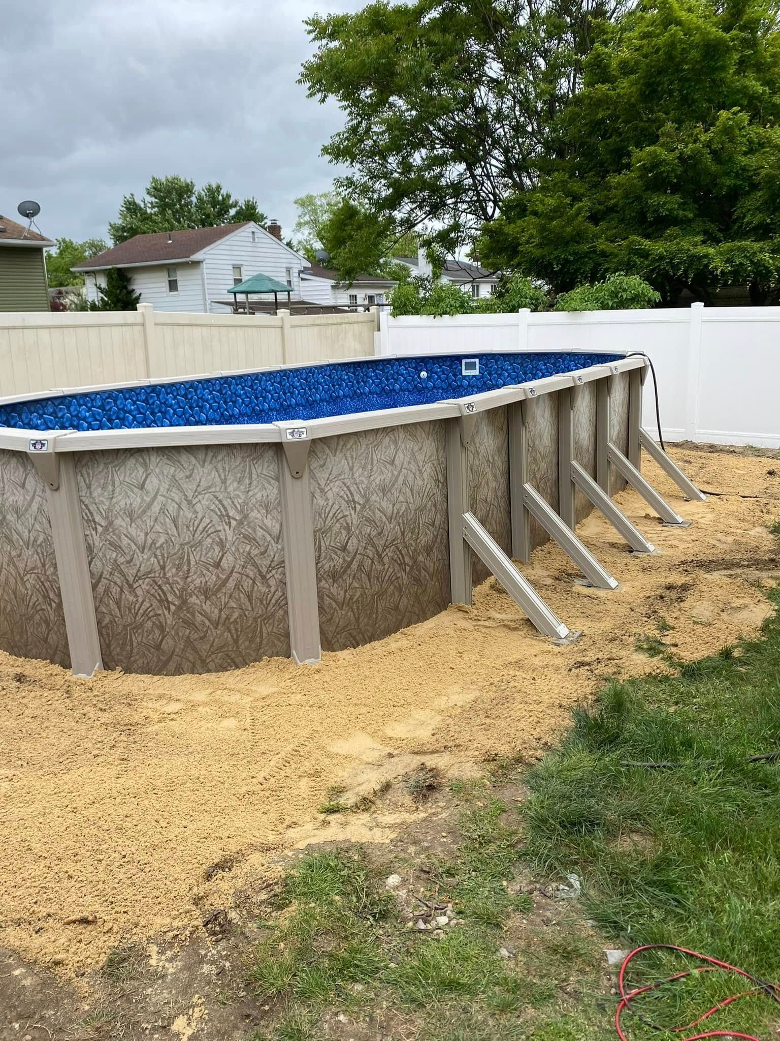 A large swimming pool is sitting in the dirt in a backyard.